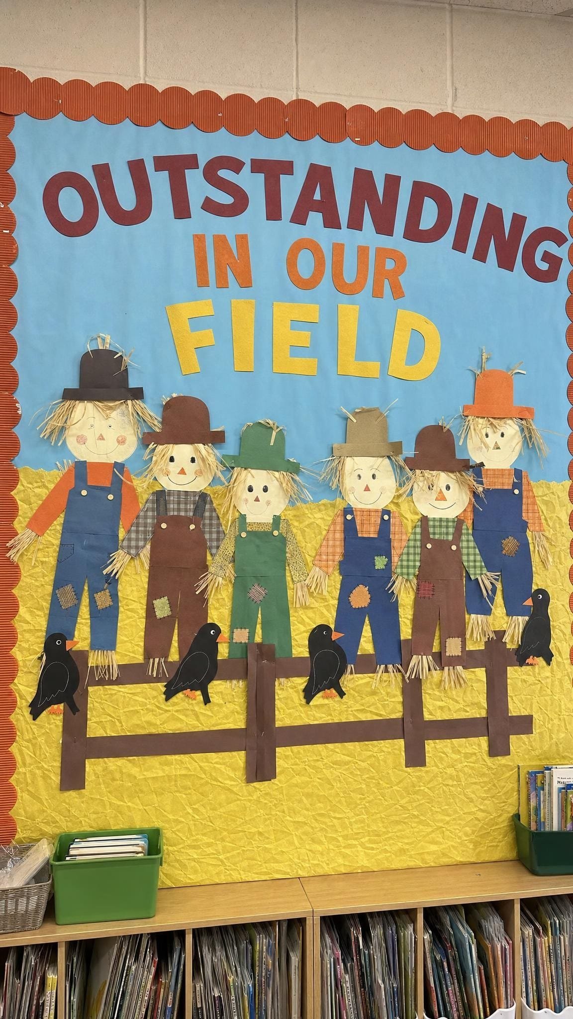 Bulletin board with children's paper scarecrow self portraits in a paper hay field