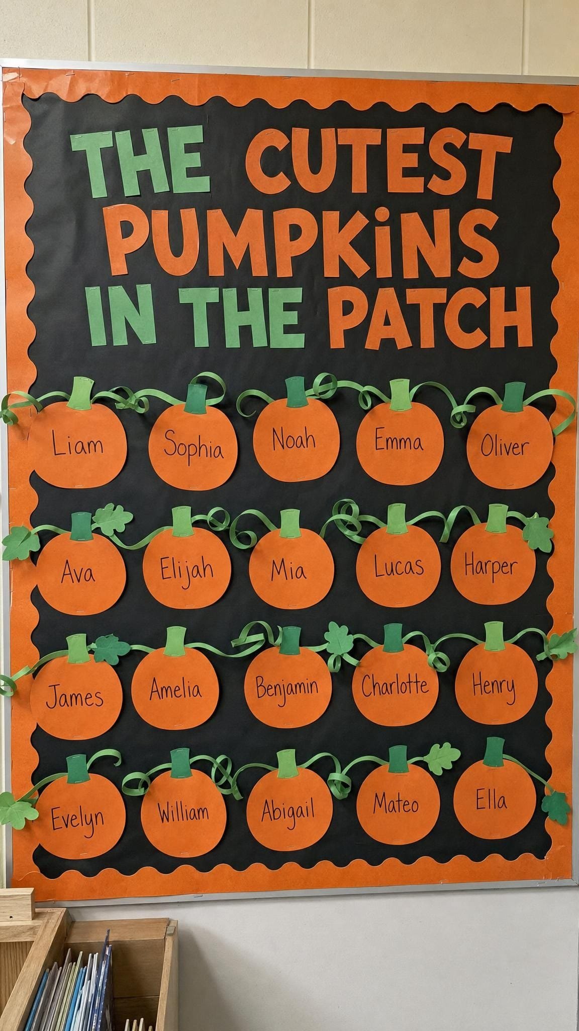 Black bulletin board with rows of orange paper pumpkins each labelled with a child's name