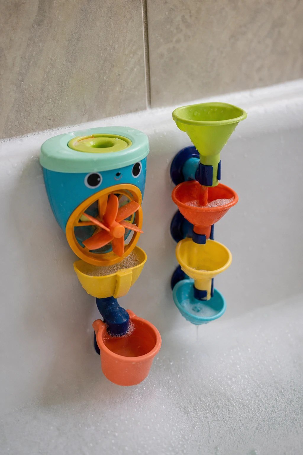 A colorful bath toy with cups and a water wheel on a bathtub