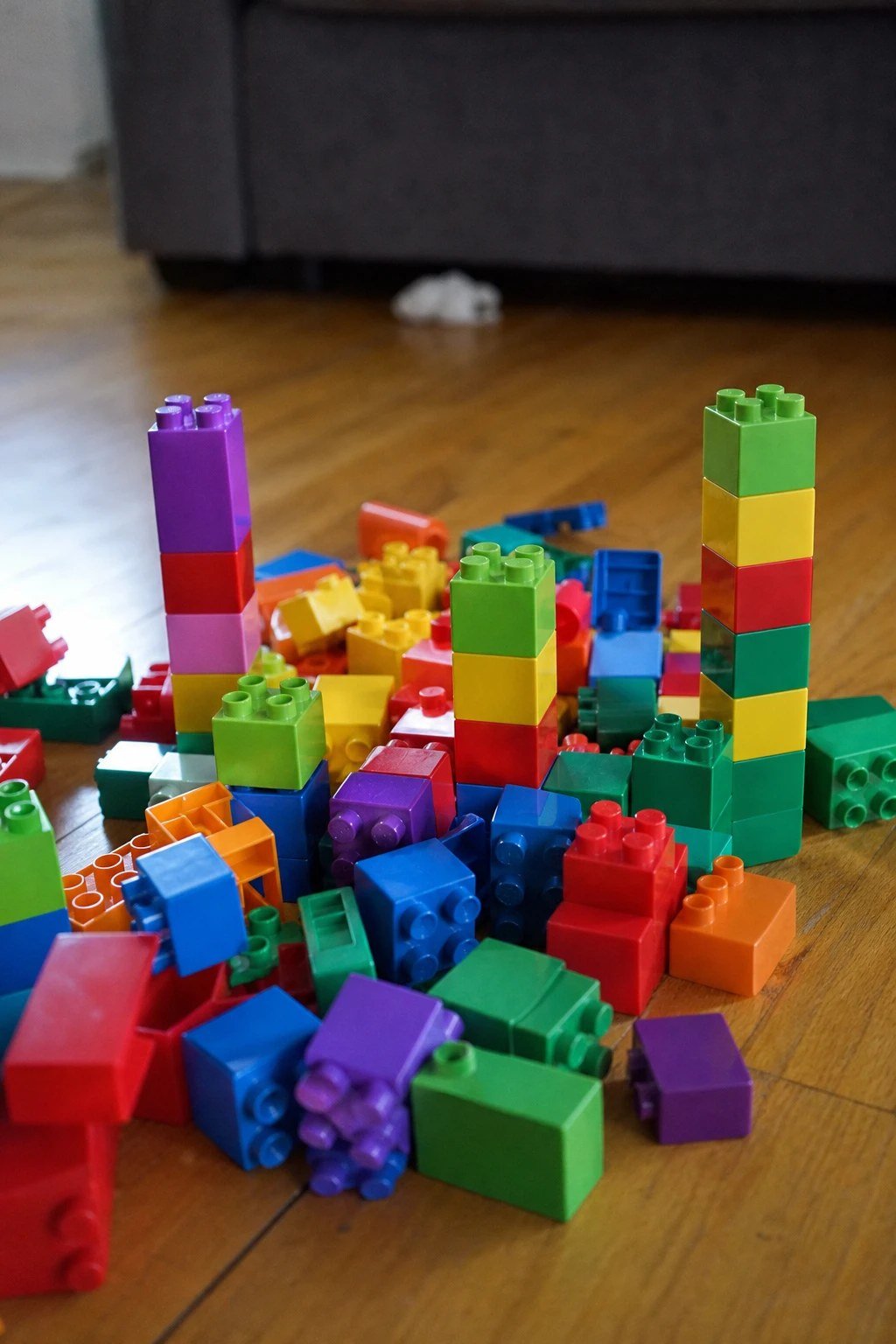 Large chunky toddler building bricks stacked into towers on a wooden floor